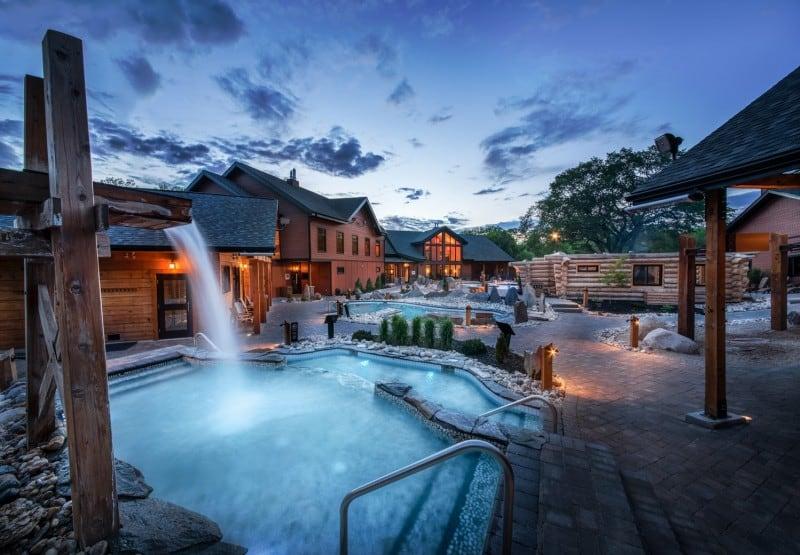 Thermea Spa Village in Winnipeg, Manitoba, with steaming outdoor thermal pools, a waterfall and timber-framed cabins at dusk