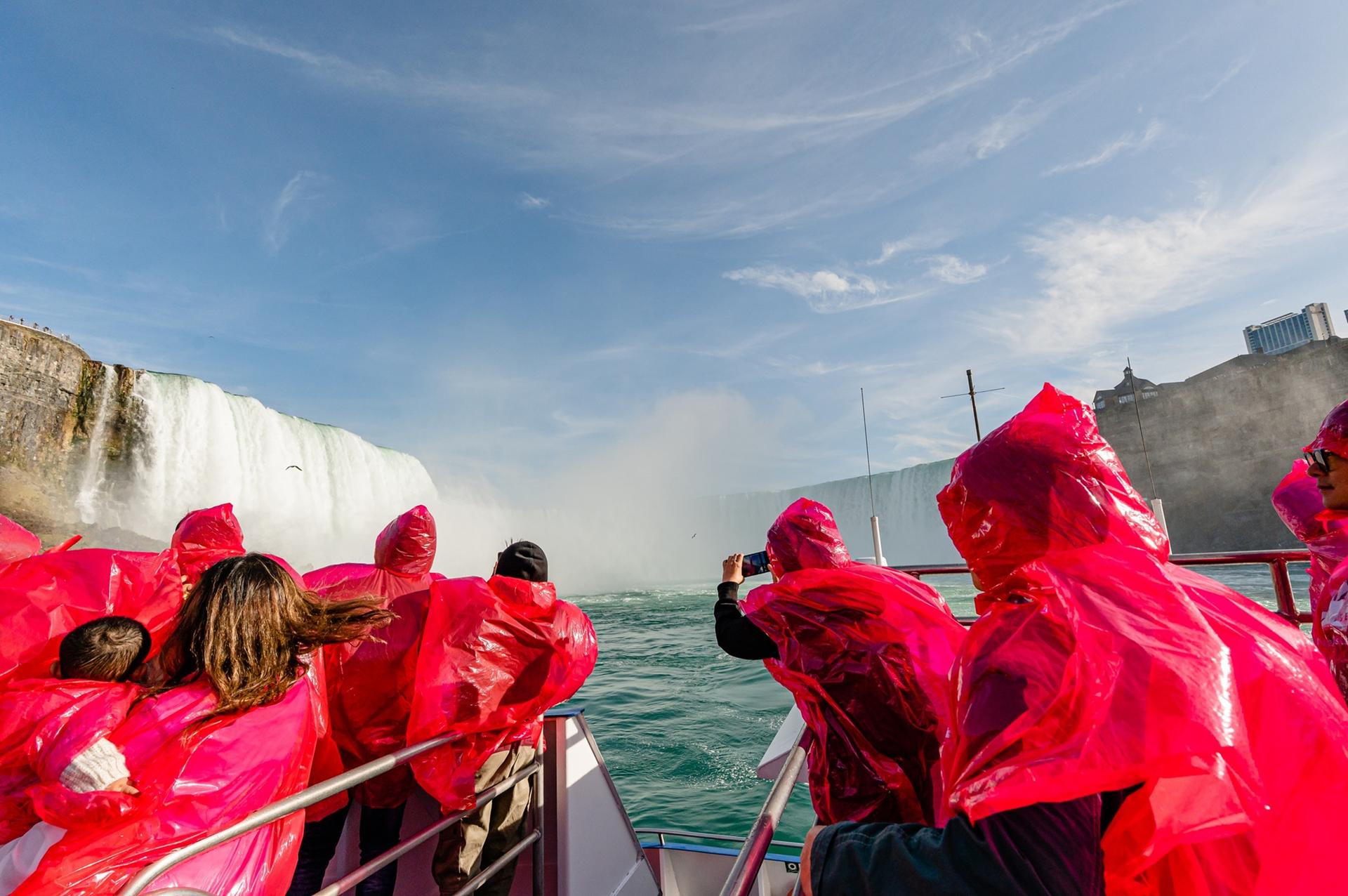 People in red rain ponchos viewing a large waterfall from a boat