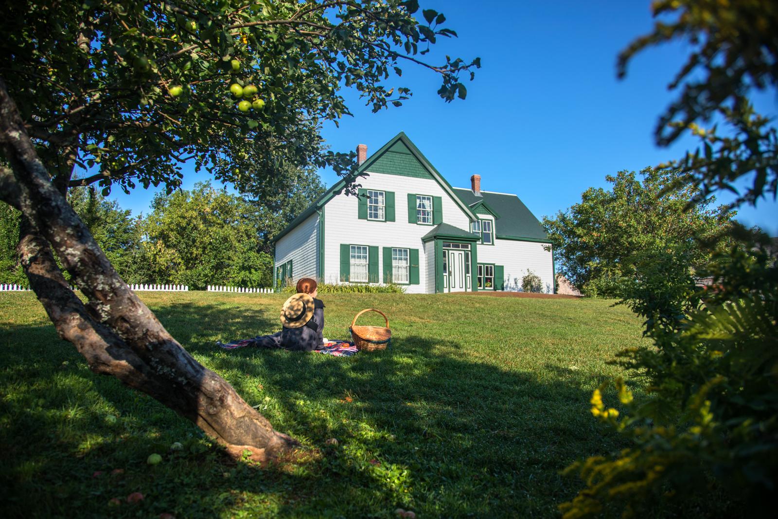 Person sitting on a lawn in front of a white and green farmhouse