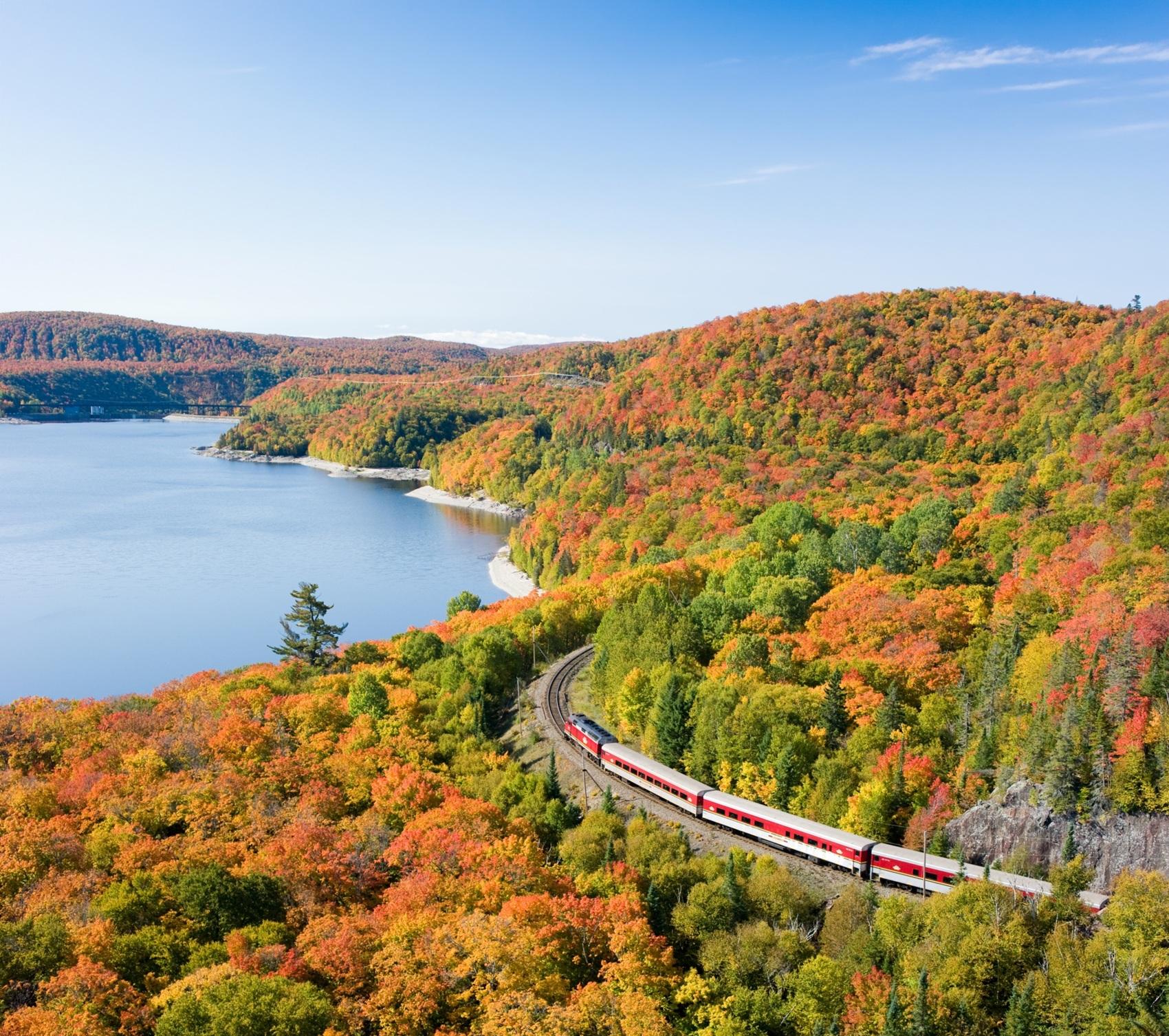 Train travelling through colourful autumn forest beside a lake
