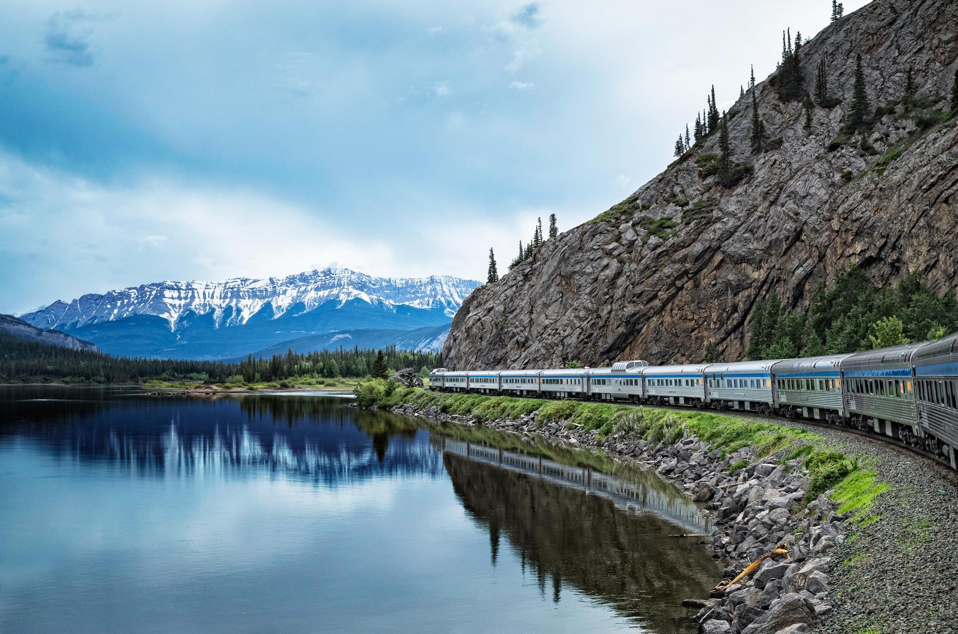Passenger train travelling beside a mountain lake and rocky cliffs
