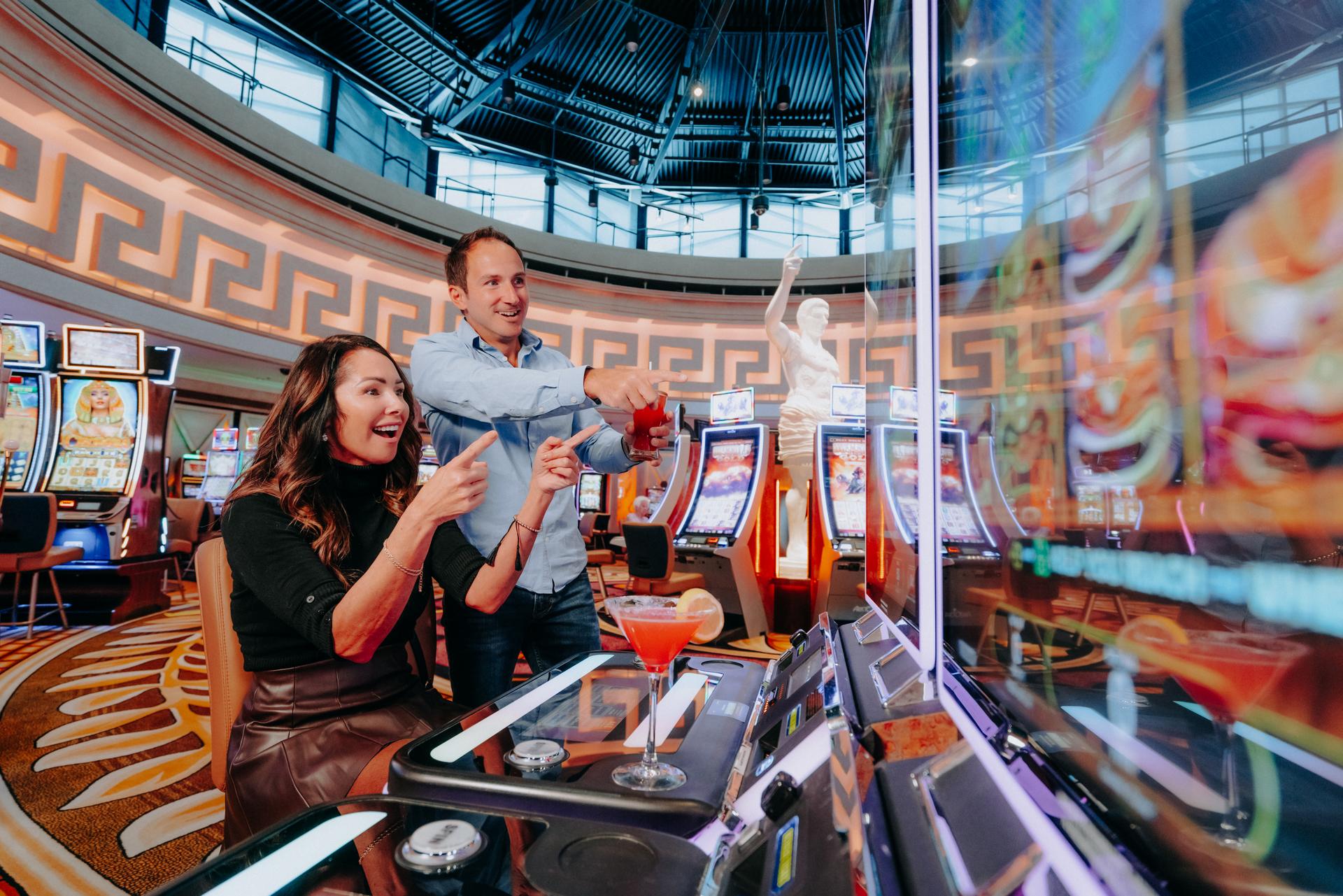 Caesars Windsor casino gaming floor in Windsor, Ontario, with two people playing slot machines beneath a domed ceiling and Roman-style statuary