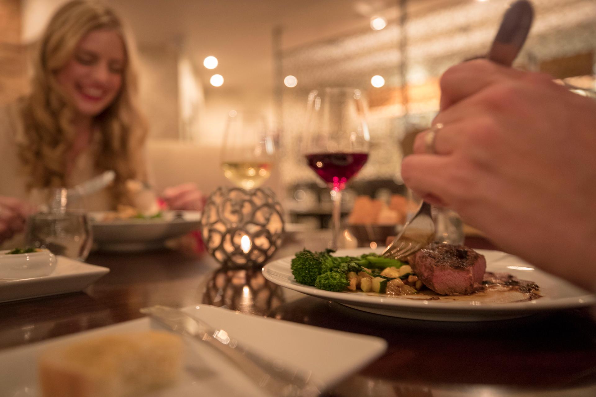 Hockley Valley Resort dining room in Mono, Ontario, with two people sharing a candlelit dinner of seared meat and broccolini paired with red and white wine