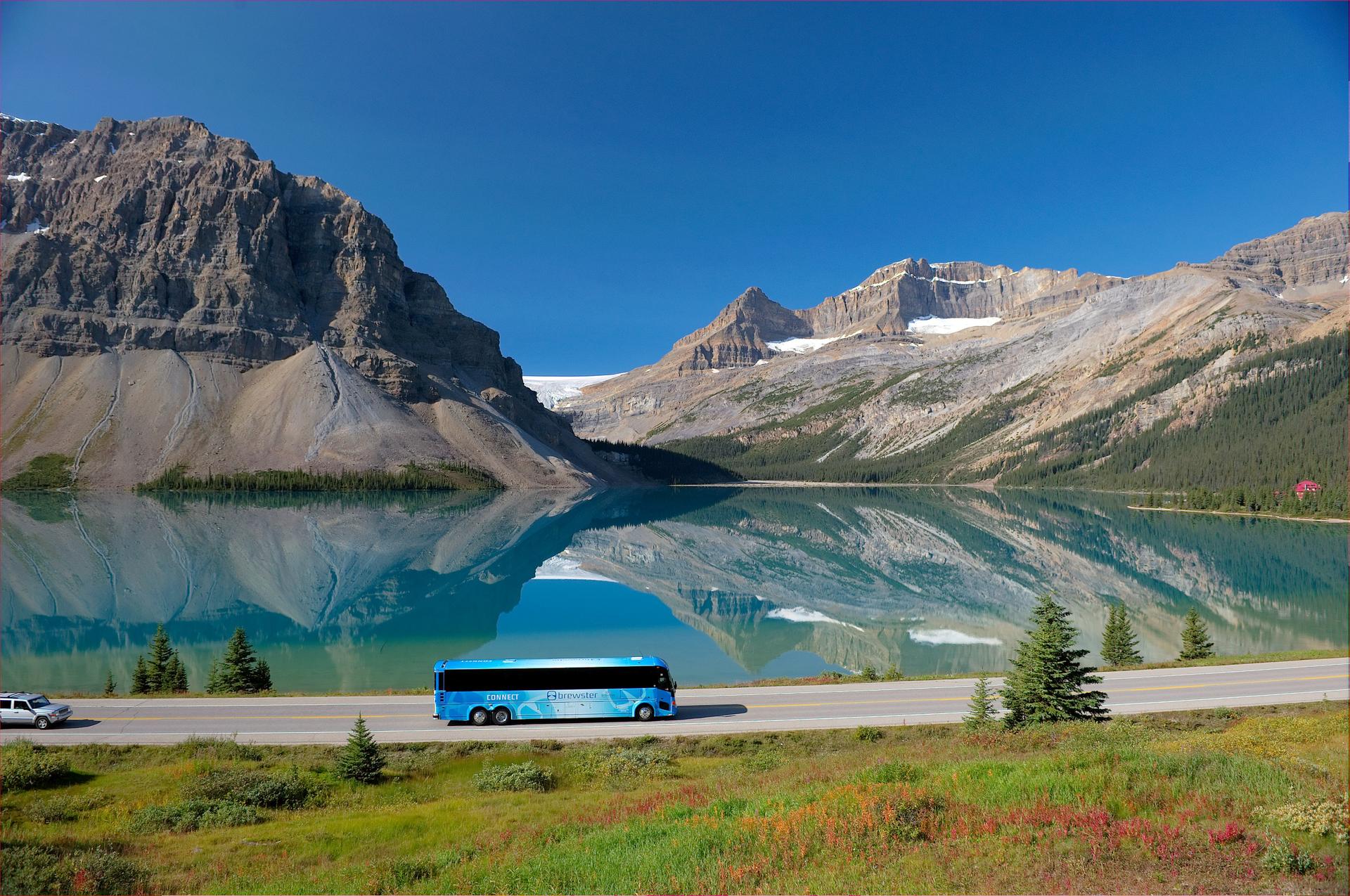 A tour bus travels the Icefields Parkway alongside the turquoise waters of Bow Lake, framed by glacier-capped peaks