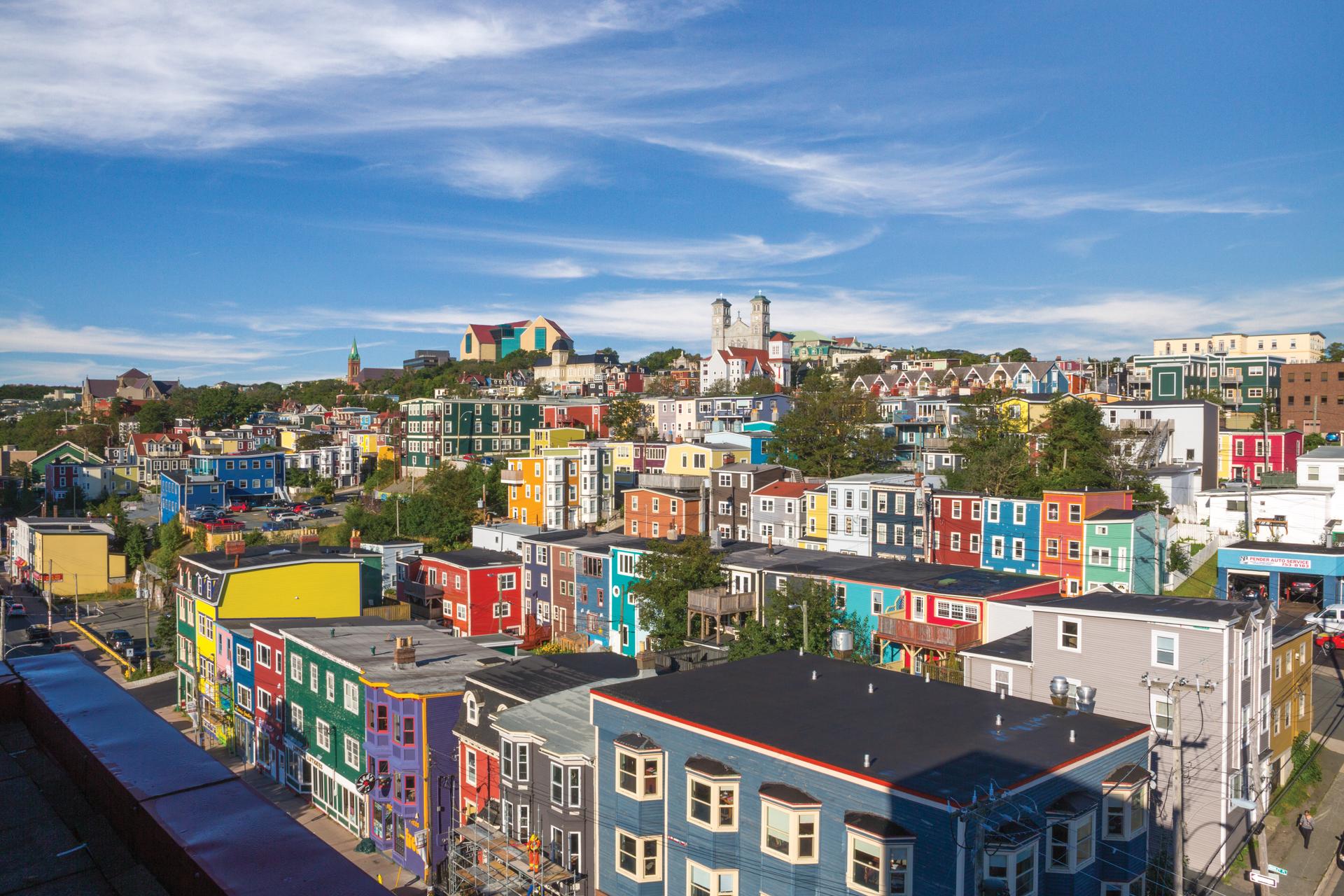 Rows of brightly coloured jellybean row houses climbing a hillside under a blue sky in downtown St. John's, Newfoundland