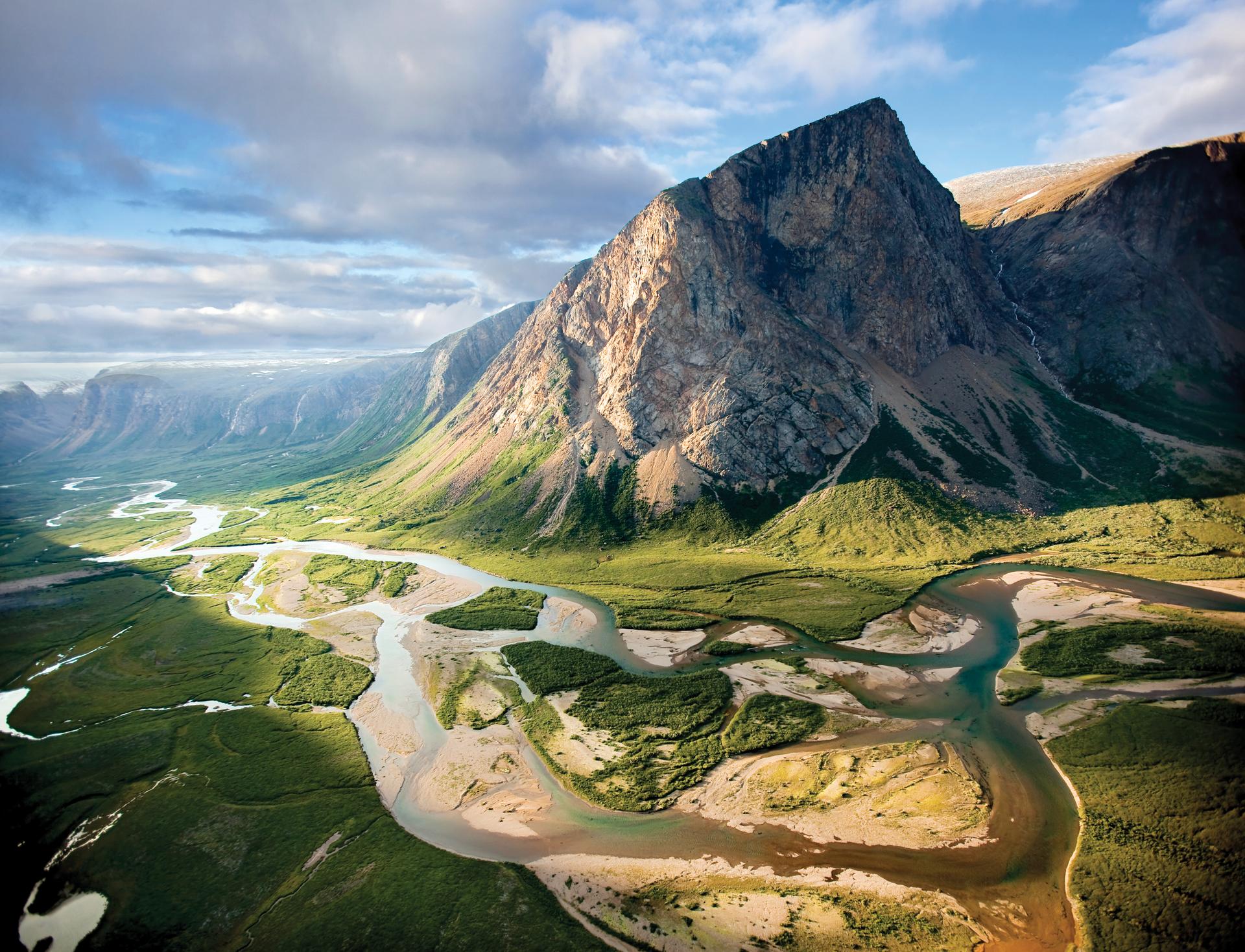 Aerial view of a towering rocky peak rising above a braided river winding through green tundra valley in Torngat Mountains National Park, Labrador