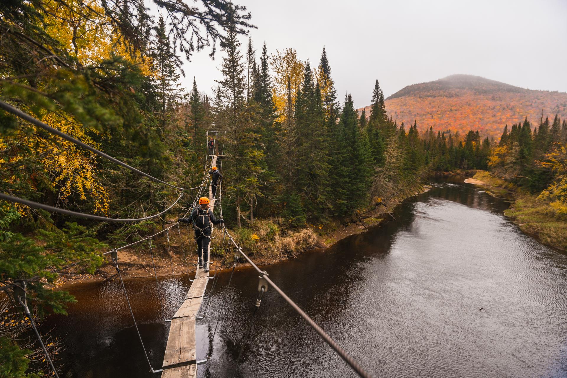 Harnessed climbers wearing helmets cross a suspended cable bridge above the Diable River on the Via Ferrata du Diable in Mont-Tremblant Provincial Park