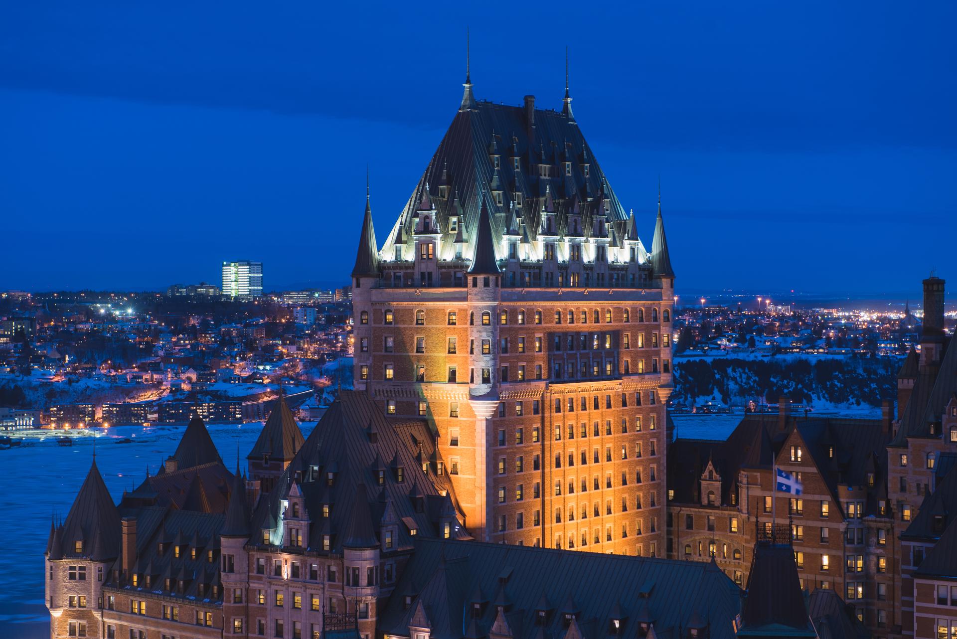 Fairmont Le Château Frontenac's illuminated central tower and turreted rooftops rising above snow-covered Québec City at night