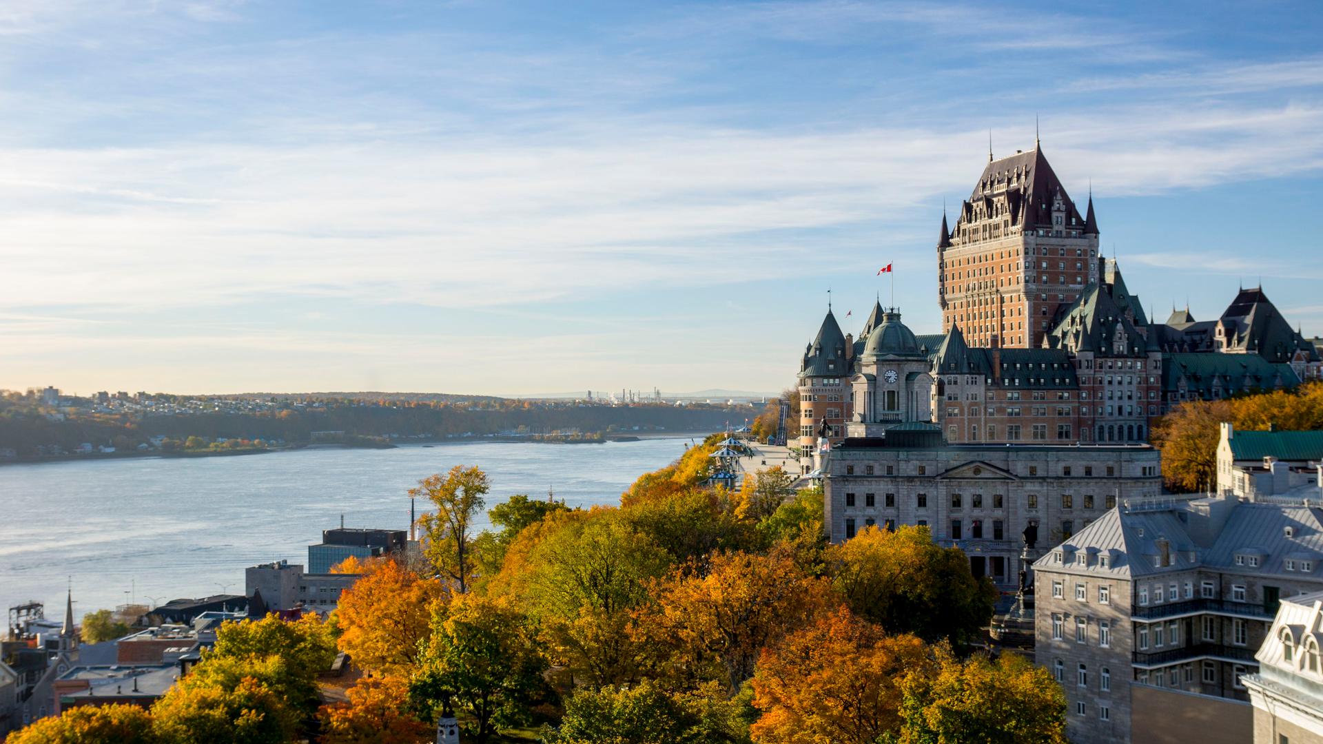 Fairmont Le Château Frontenac's turreted rooftops rising above autumn foliage overlooking the St. Lawrence River in Old Québec
