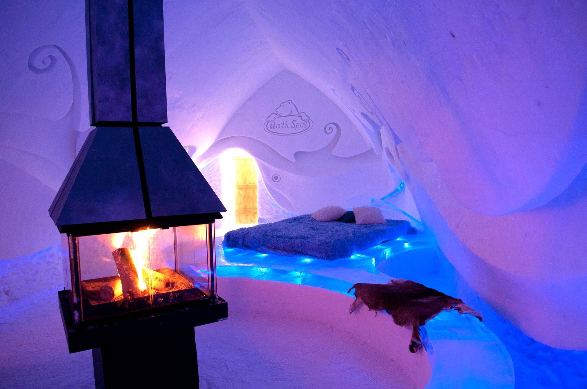 Blue-lit themed room at Hôtel de Glace with a glass-enclosed fireplace, fur-topped ice bed and carved snow walls