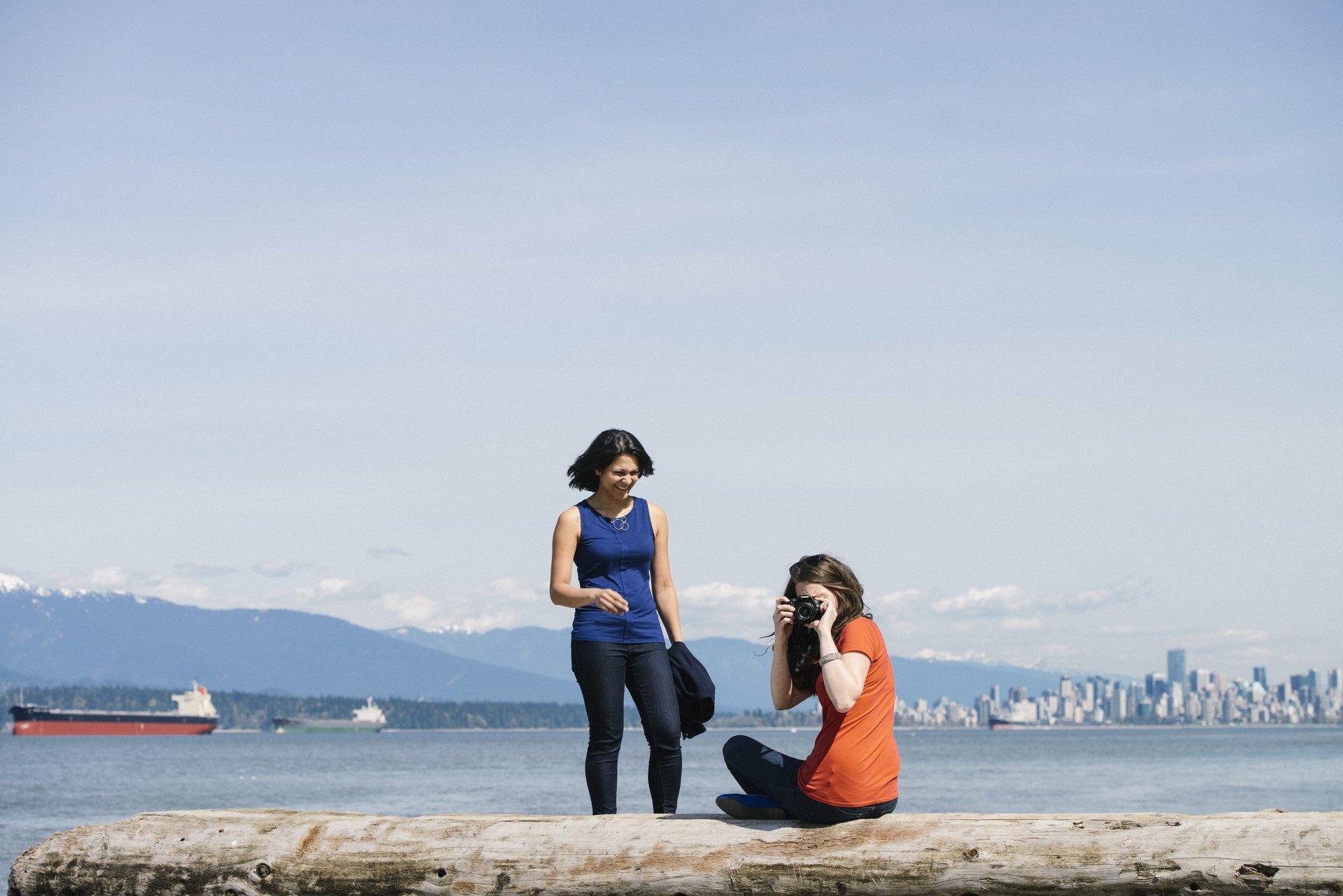 two people sitting on a log at the beach with water views behind them