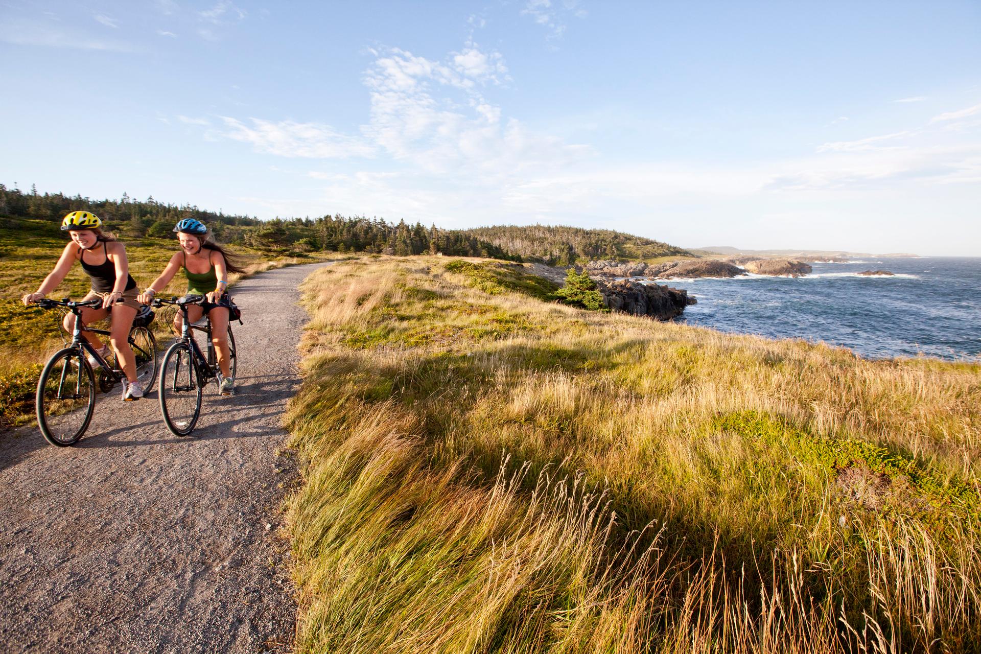 Two people cycling on a gravel path along the ocean in Cape Breton Highlands National Park