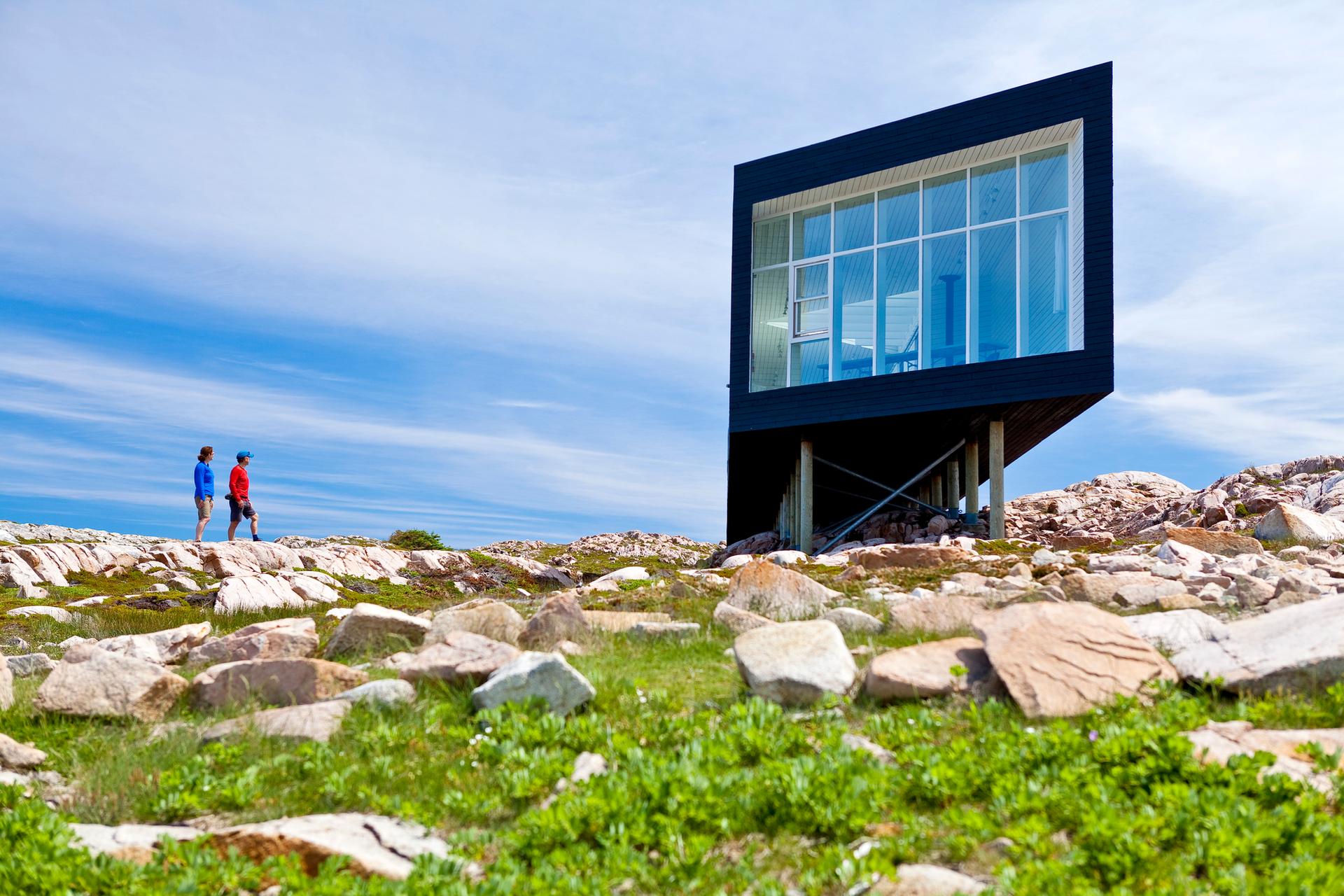 Two people walking along a rocky outcrop taking in the view of the Fogo Island Inn
