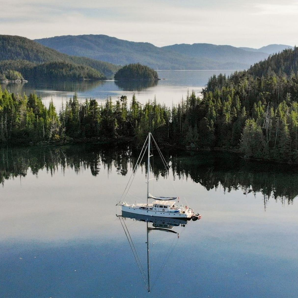 A sailboat sits anchored in an ocean inlet surrounded by green forested islands.