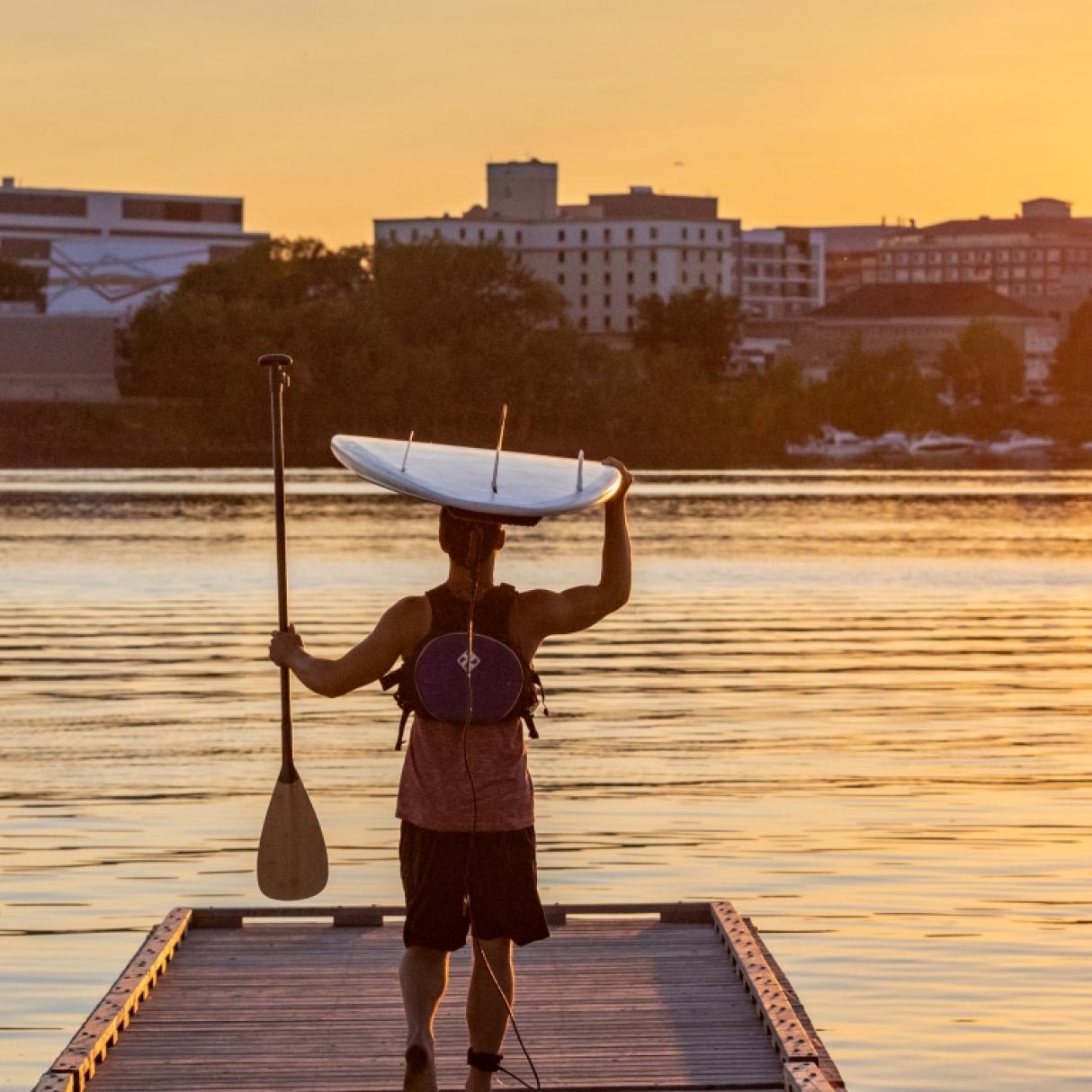 A person prepares to launch their paddleboard at dawn in Fredericton