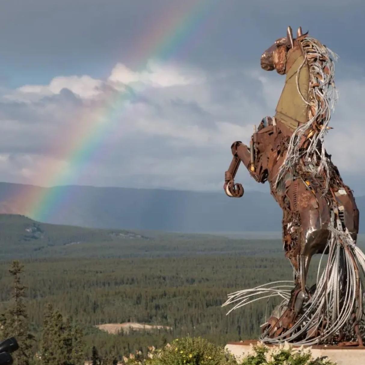 A statue of a leaping horse behind a rainbow-streaked sky in Whitehorse