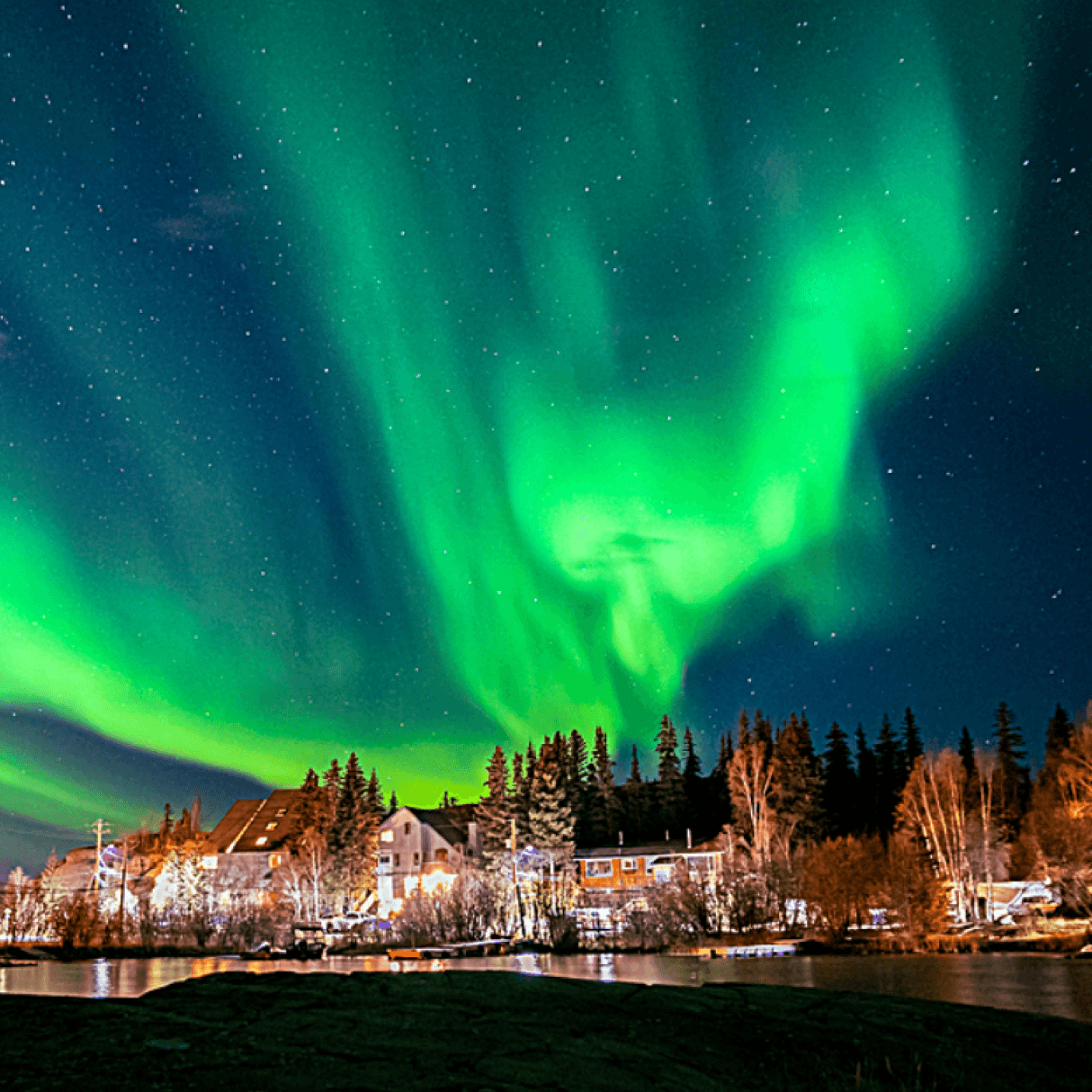 Green aurora borealis light up the night sky above a small town.