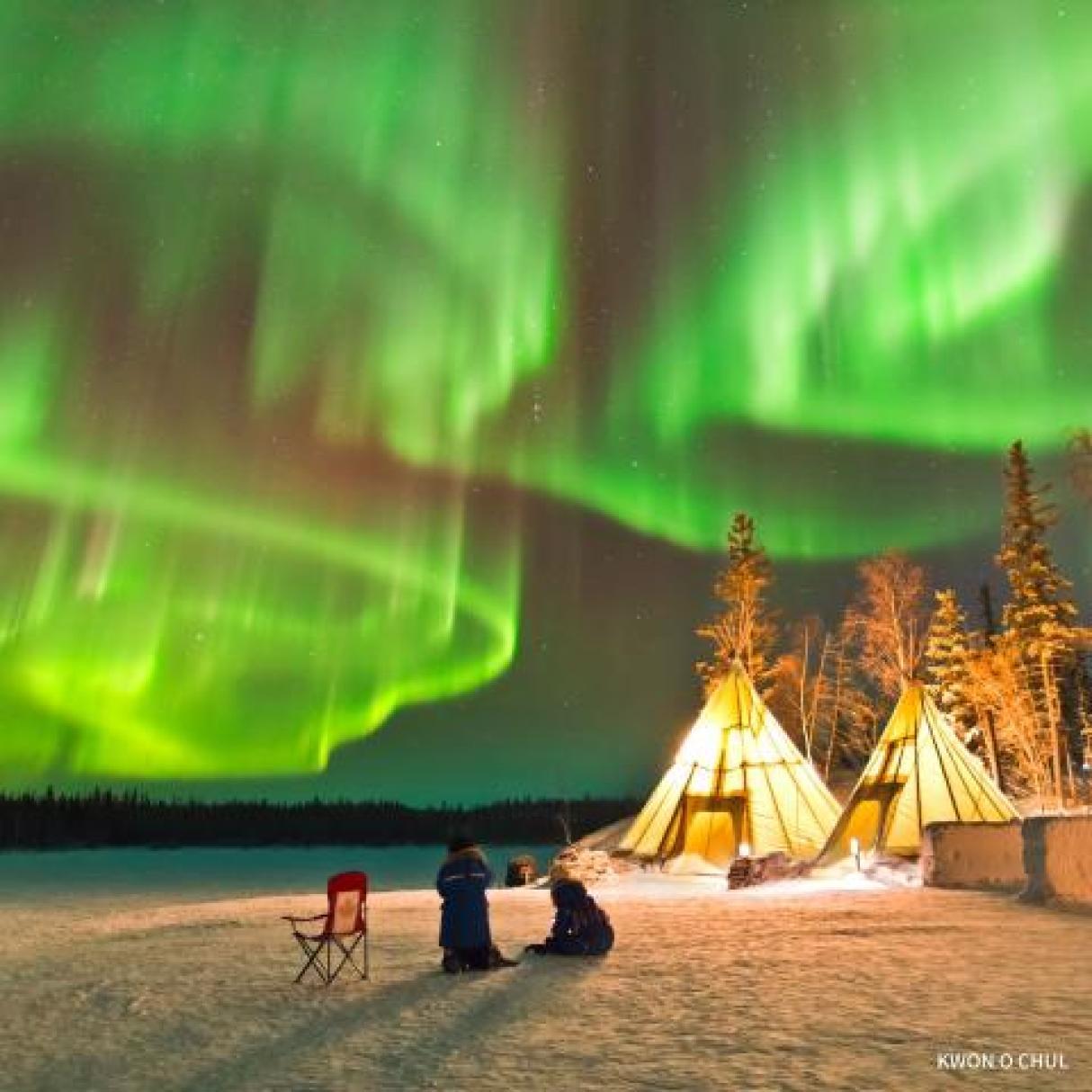 Teepees under bright green northern lights