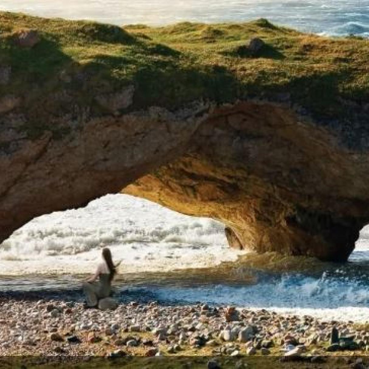 A person on the beach beneath unusual rock arches