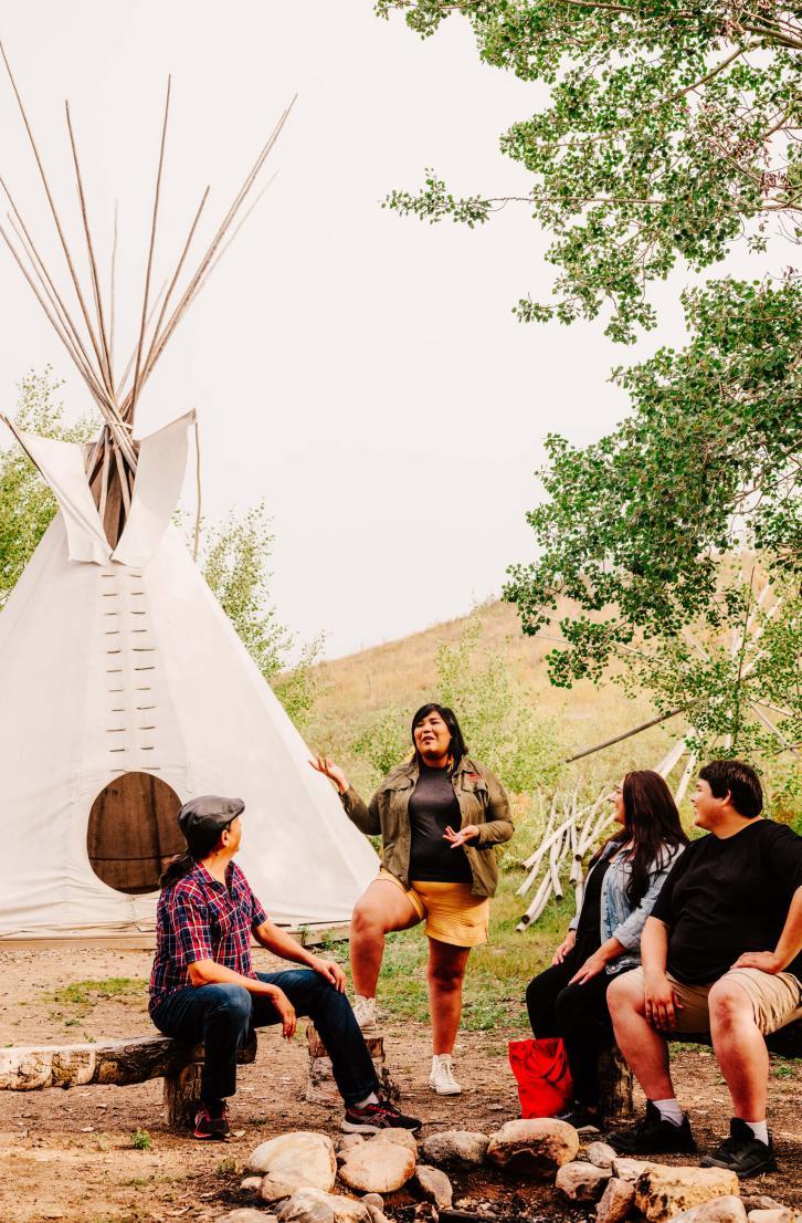 An indigenous person speaks with tourists at a camp, outisde a teepee