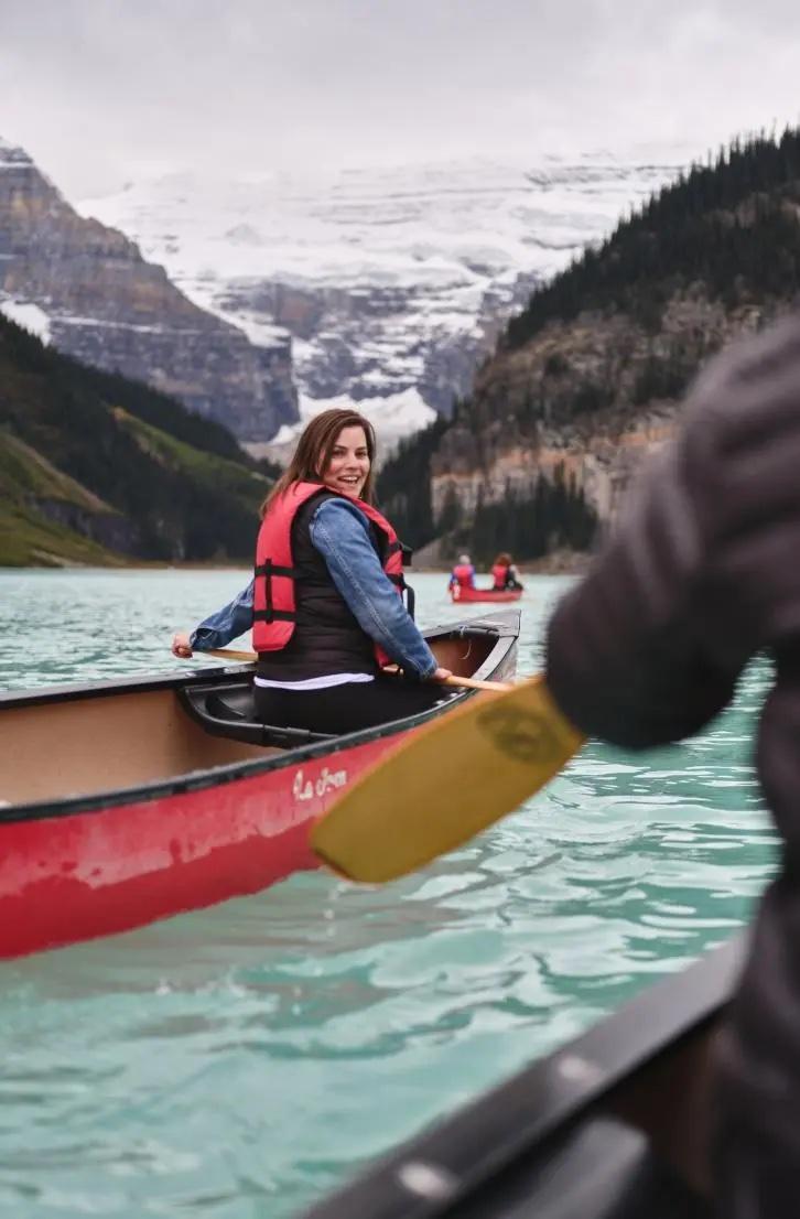 A woman looks back as she paddles a canoe on a pristine lake