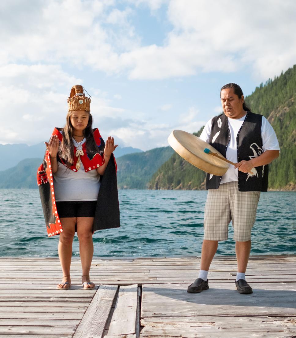 An Indigenous man and girl playing a drum on a dock in Canada