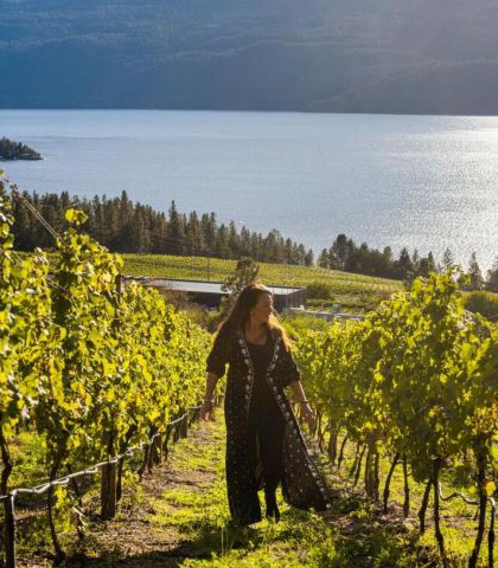 A woman walks through a vineyard by a lake